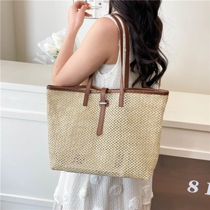 Large straw tote bag with brown leather handles worn by a model in a summer dress