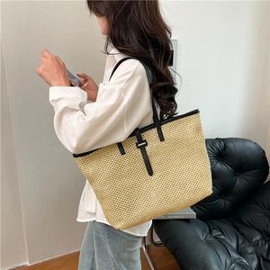 Large straw tote bag with black leather straps shown on model for summer beach vacations