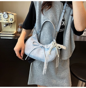 Detail of light blue crescent leather bag with lace pearl charm and delicate bow accent