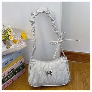 Détail du sac sous l'aisselle argenté plissé avec papillon métallique et bride à nœud