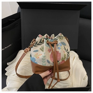 Detail of drawstring bucket bag with floral embroidery and brown leather trim