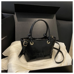 Detail of black glossy cracked leather tote with embossed logo and gold metal hardware