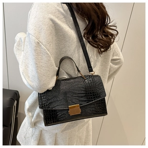 Detail of black crocodile pattern handbag worn by a model with gold metal lock buckle