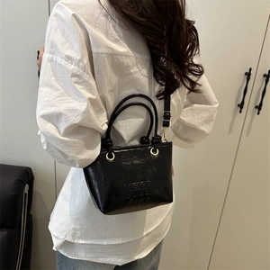 Stylish black trapezoid bucket bag with embossed letters and adjustable shoulder strap