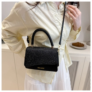 Detail of black glitter small crossbody bag with gold logo on a home interior background