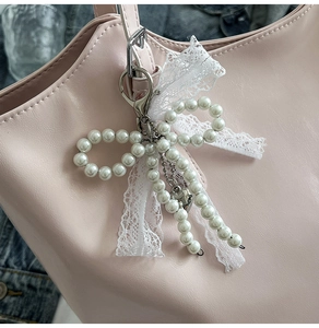 Detail of pearl bow bag charm with lace and silver heart on pink leather tote bag