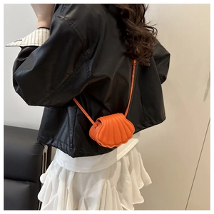 Detail view of mini orange shell-shaped crossbody bag with pleated texture on a model