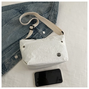White textured crossbody bag with adjustable strap shown next to a smartphone for scale