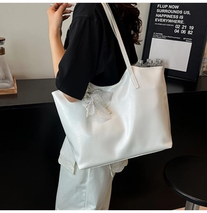 Detailed view of white oversized tote bag with lace and pearl bow charm on shoulder strap