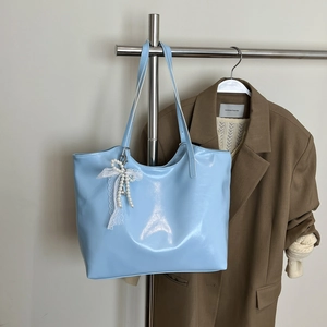Detail of light blue patent leather tote bag featuring white lace pearl bow pendant