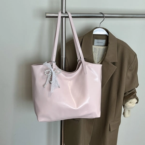 Detail of glossy pink tote bag featuring a white lace bow and elegant pearl charm