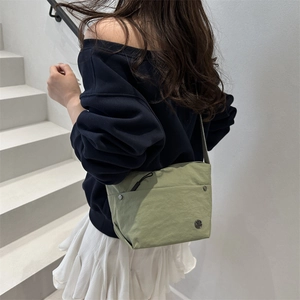 Grass green nylon crossbody bag with wide shoulder strap and metal logo on white stairs