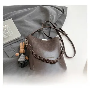 Detail of vintage brown bucket bag with woven handle and plaid rabbit charm on grey blazer