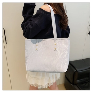 Detail of white textured tote bag featuring gold rivet studs and slender shoulder strap
