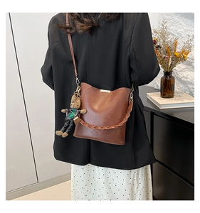 Detail of brown leather bucket bag with woven handle and cute plush bear charm