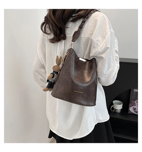 Detail of dark brown matte leather bucket bag with woven strap and cute bunny charm
