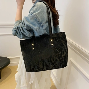 Minimalist black crinkled tote bag with gold studs shown on shoulder for daily commute