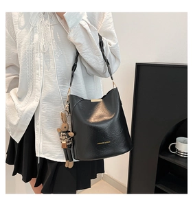 Detail of black bucket bag with braided strap and cute rabbit pendant in minimalist studio