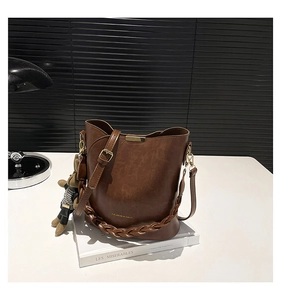 Detail of dark brown bucket bag with braided strap and cute bear charm on a book