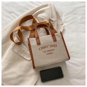 Flat lay of canvas tote bag with brown leather trim on beige blazer and mobile phone