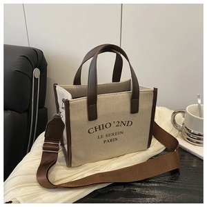 Detail of canvas tote bag featuring premium brown leather handles and brand lettering
