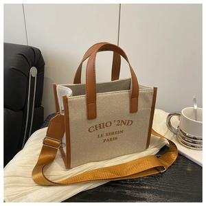 Detail of beige canvas tote with brown leather handles and chic orange shoulder strap
