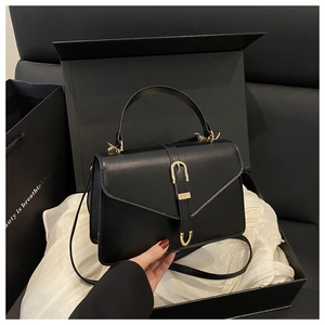 Detail of a black leather crossbody bag with gold buckle in a gift box with a white cloth