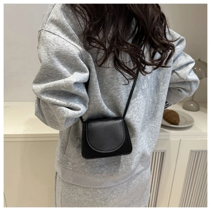 Details der schwarzen Mini-Umhängetasche mit Litschi-Struktur über grauem Hoodie
