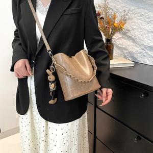 Modern vintage brown bucket bag with woven handle and cute plush charm on shoulder