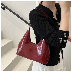 Close-up of a glossy dark red patent leather hobo bag styled on a model's shoulder