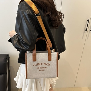 Chic canvas tote bag with brown leather handles worn crossbody by a model in black leather