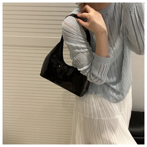 Detail of glossy black patent leather shoulder bag showing its mirror finish and curved base