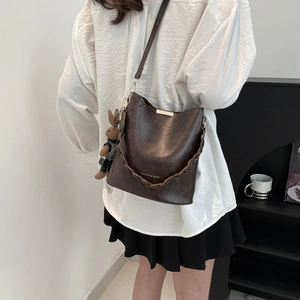 Deep brown leather bucket bag with woven handle and plush rabbit charm on a white background