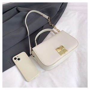 Detail of cream crossbody bag with gold square buckle and leather chain strap on fabric