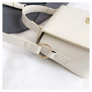 Close-up of golden metal rings and fine stitching on a beige leather shoulder bag