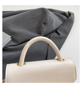 Détail d'un sac à main beige en cuir texturé avec anneaux métalliques dorés et poignée