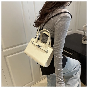 Detailed view of off-white lychee grain leather handbag with silver twist lock and strap