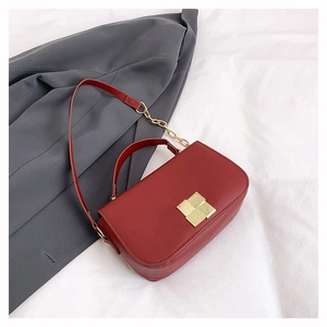 Close-up of burgundy square flap bag with gold metal lock on a grey suit background