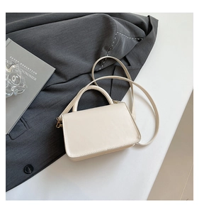Détail d'un sac bandoulière crème minimaliste avec boucle dorée sur fond blanc