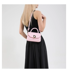 Détail d'un sac à bandoulière rose avec boucle métallique en D dorée et texture en cuir