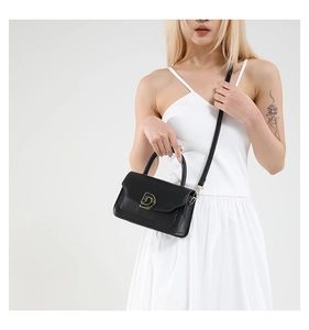 Détail d'un sac à main chic en cuir noir avec boucle dorée en D et garnitures en métal
