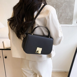 Classic black leather square crossbody bag with gold buckle on a white suit model