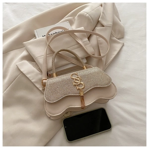 Detail of a beige textured handbag with gold SS clasp and long tassel on a suit jacket