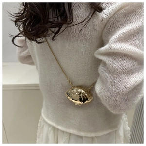 Detail of a mini gold shell-shaped crossbody bag with a sleek metallic finish and chain