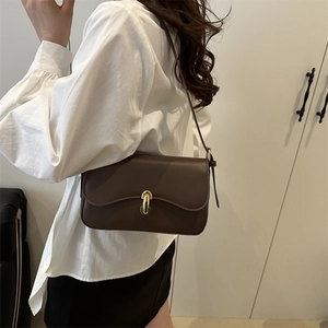 Minimalist dark brown leather shoulder bag with gold U-shaped buckle on a female model