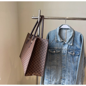 Detail of a large brown tote bag featuring a vintage M-letter monogram and slim handles