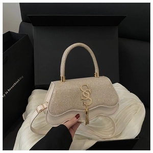 Detailed view of cream crossbody bag with gold glitter flap and metal SS logo pendant
