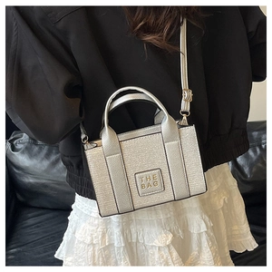 Nahaufnahme einer silbernen Metallic-Einkaufstasche mit The Bag-Schriftzug auf Ledersofa