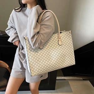 Large off-white tote bag with M-pattern print and rivets shown on a stylish model