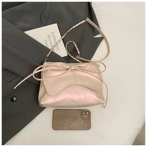 Detail of champagne pink satin handbag with large bow and metal chain strap beside phone